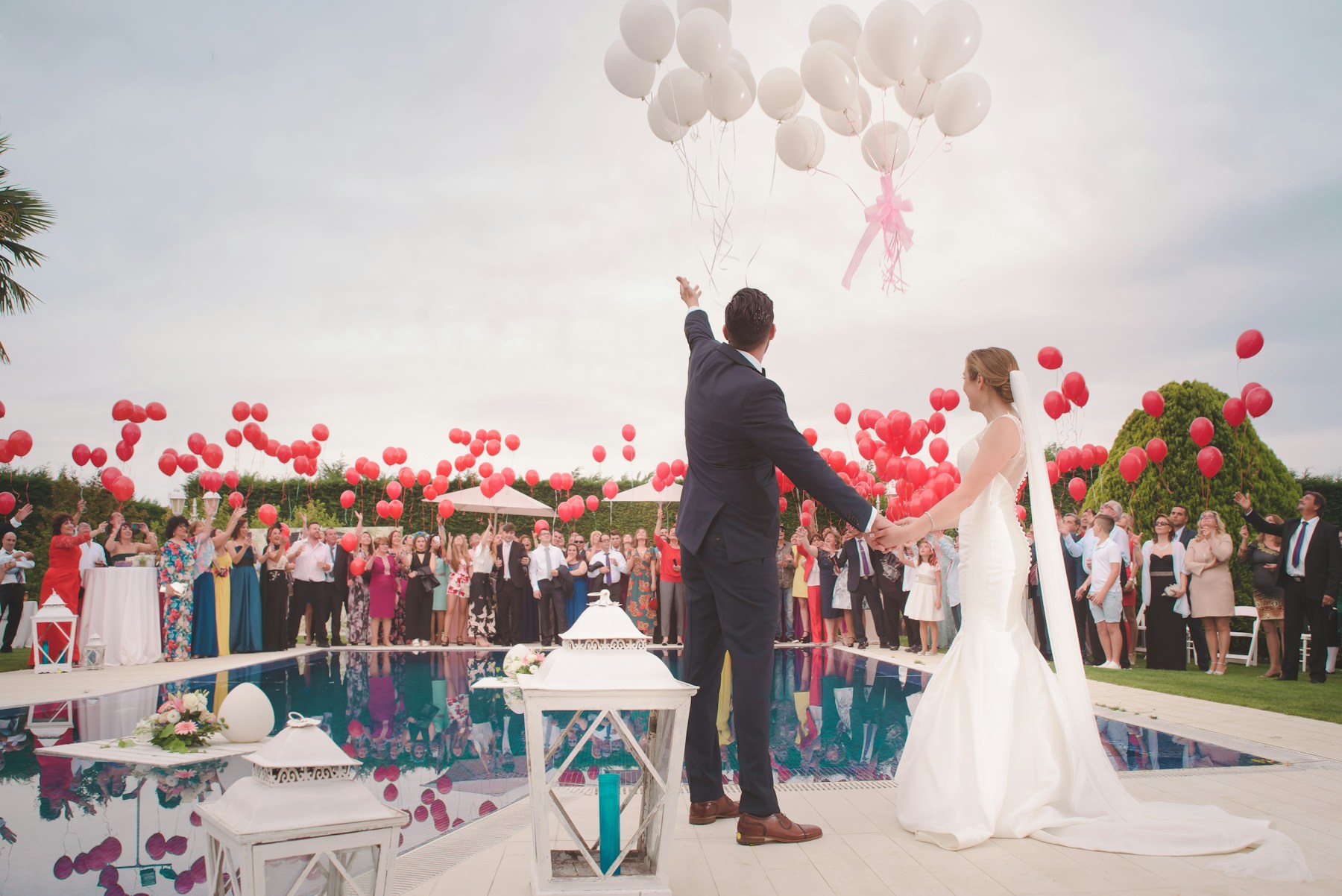 A stock wedding couple releasing balloons beside a swimming pool